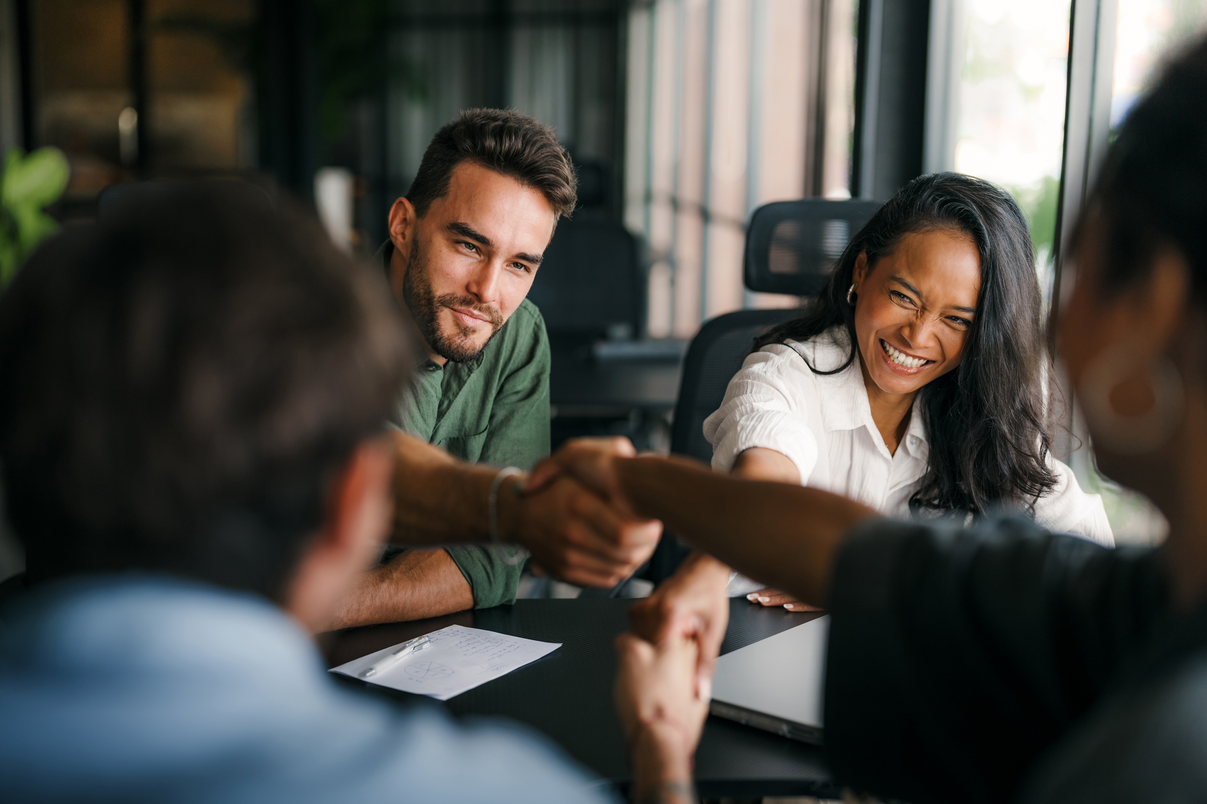 Varias personas en una sala de reuniones se dan la mano alrededor de una mesa.